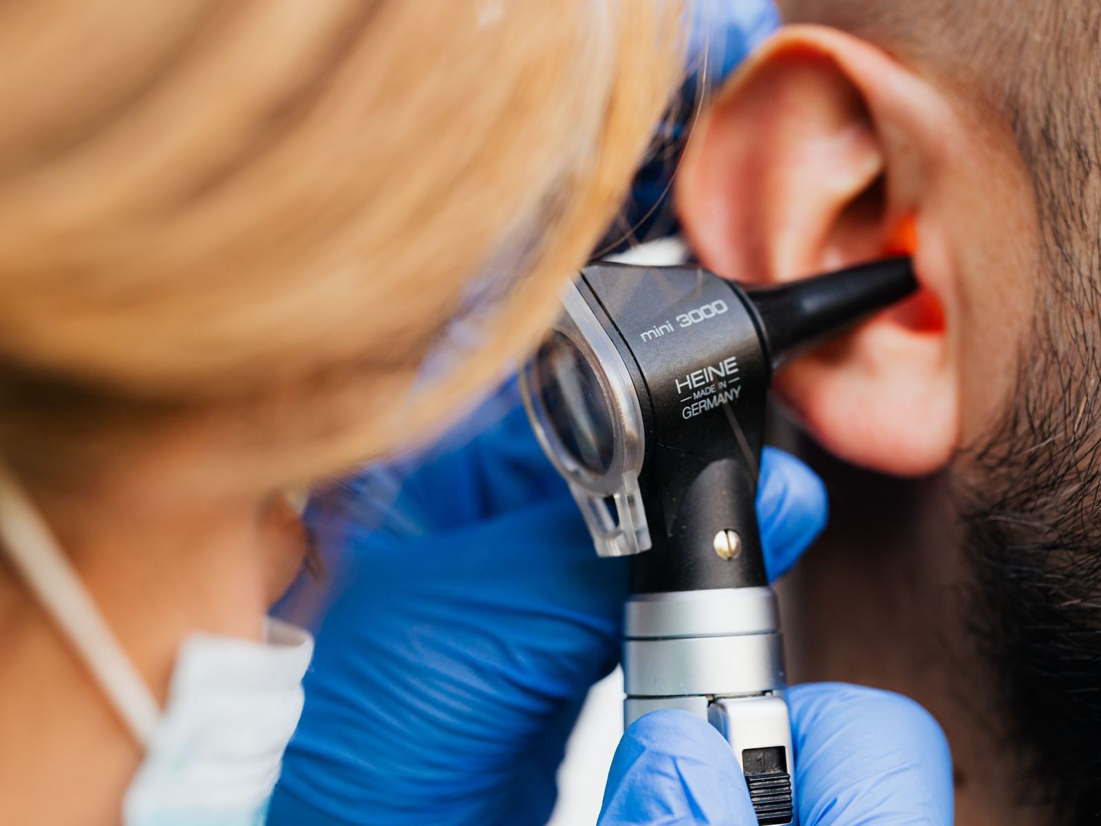 A practitioner sat by an older patient's chair at home, gently checking the ear with an otoscope.